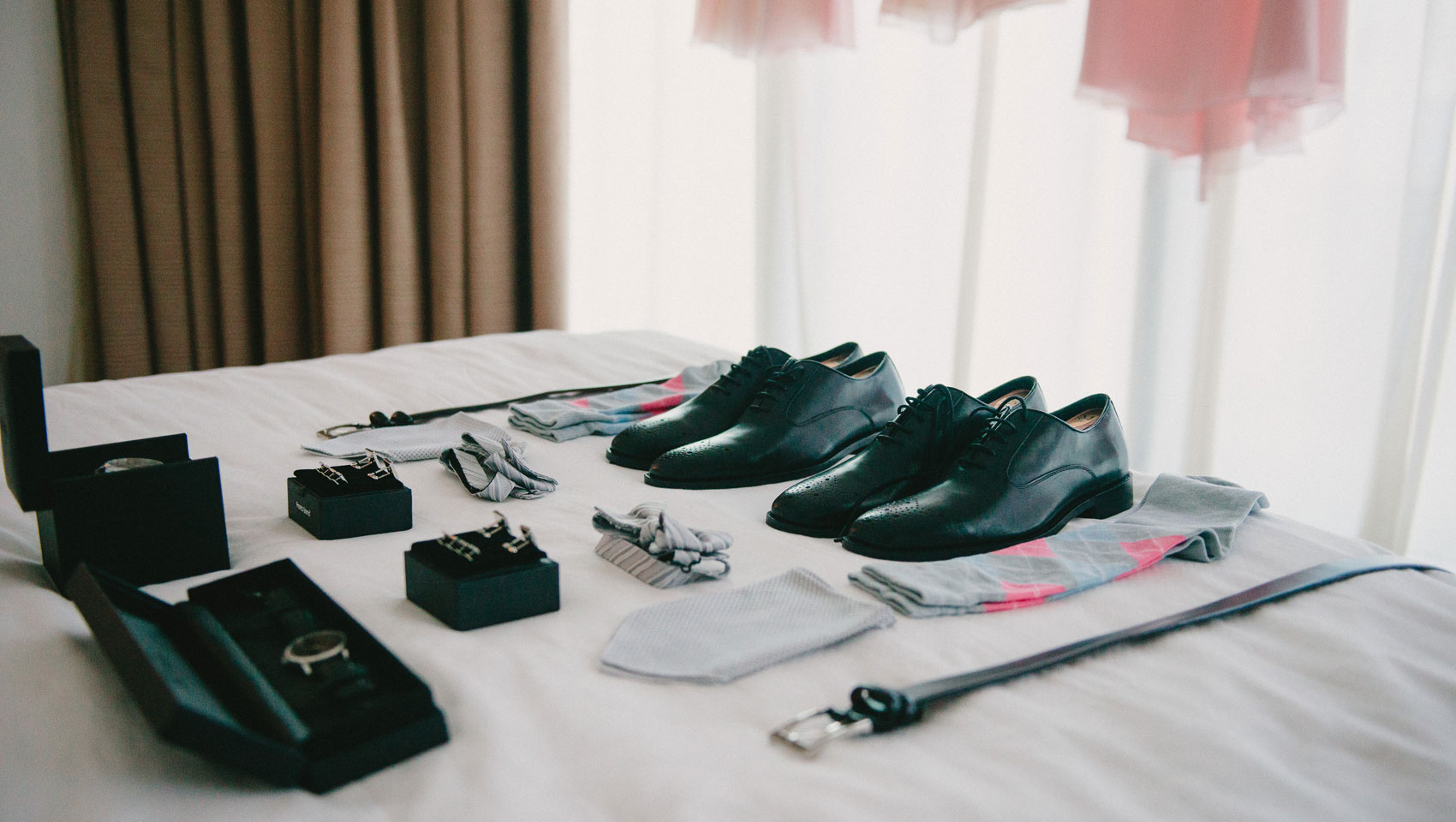 Wedding shoes, watch, tie, and belt on bed.